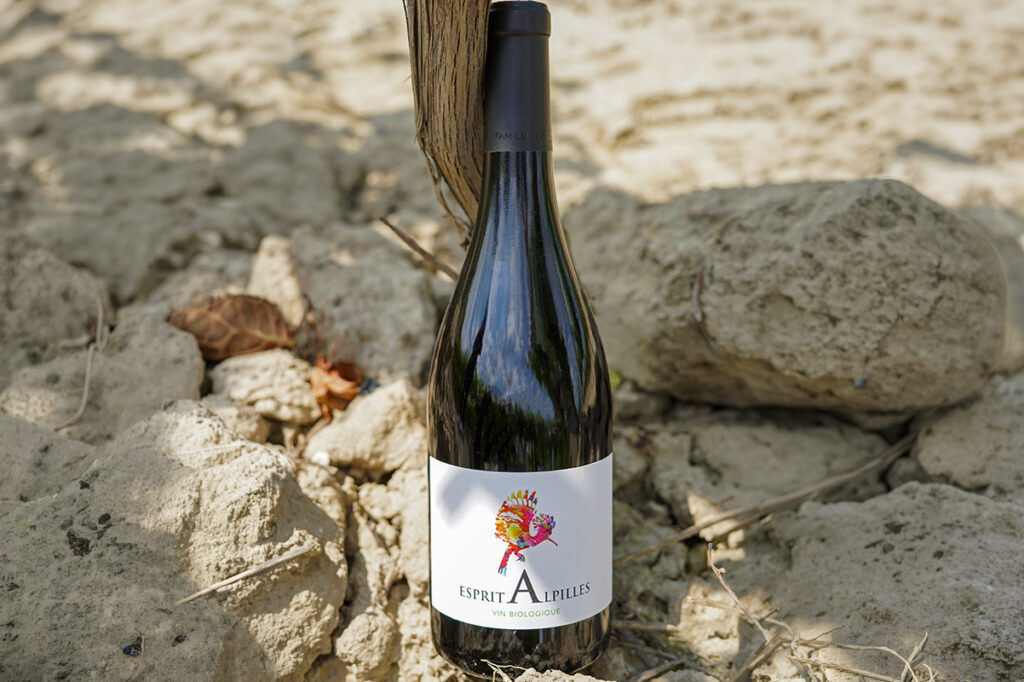 Bouteille de vin rouge bio Esprit Alpilles posée devant des pierres, avec une huppe fasciée sur l’étiquette